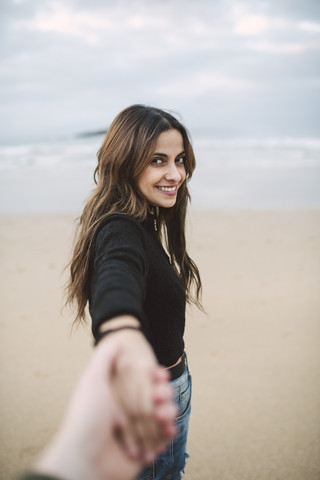 Porträt einer glücklichen jungen Frau, die am Strand ihre Hand hält, lizenzfreies Stockfoto