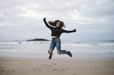 Glückliche Frau, die am Strand in die Luft springt - RAEF01698