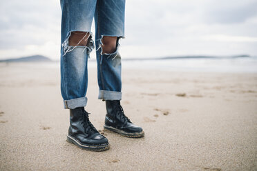 Frau in Stiefeln und zerrissenen Jeans am Strand, Teilansicht - RAEF01703