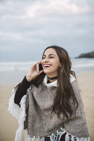 Porträt einer glücklichen jungen Frau beim Telefonieren am Strand, lizenzfreies Stockfoto
