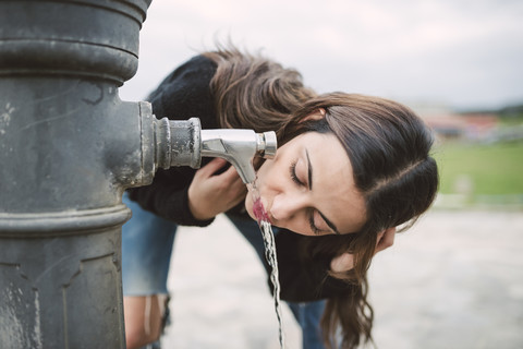 Junge Frau trinkt Wasser aus einem Brunnen, lizenzfreies Stockfoto