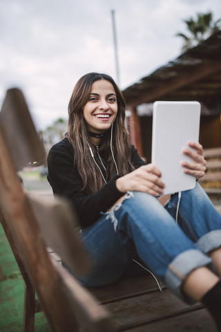 Porträt einer lächelnden jungen Frau, die ein Tablet mit Kopfhörern benutzt, lizenzfreies Stockfoto