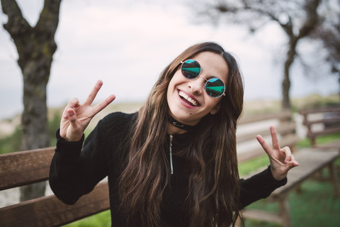 Porträt einer jungen Frau mit verspiegelter Sonnenbrille und Siegeszeichen, lizenzfreies Stockfoto