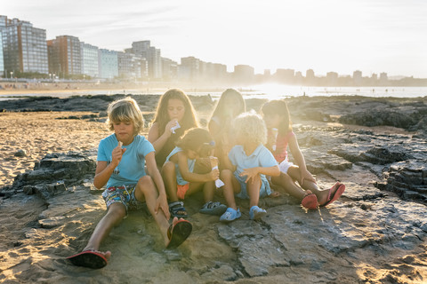 Gruppe von sechs Kindern beim Eisessen am Strand, lizenzfreies Stockfoto