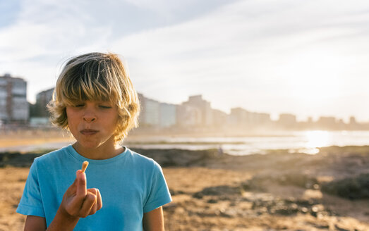 Blonder Junge isst Eiscreme am Strand bei Sonnenuntergang - MGOF02822