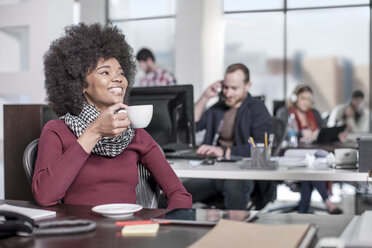 Smiling woman at desk in office drinking coffee - ZEF12544