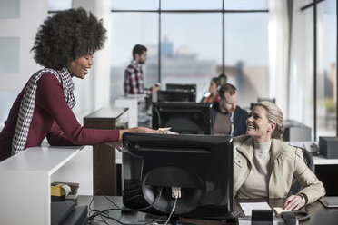 Lässige weibliche Büroangestellte, die einem Mitarbeiter hinter einem Schreibtisch mit Computer Notizen übergibt - ZEF12550