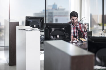 Mann am Schreibtisch im Büro schaut auf sein Handy - ZEF12566