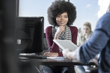 Woman at desk in office listening to coworker - ZEF12585