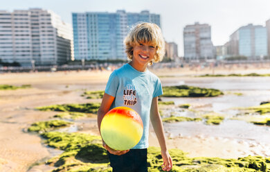 Porträt eines blonden Jungen mit Ball am Strand - MGOF02842