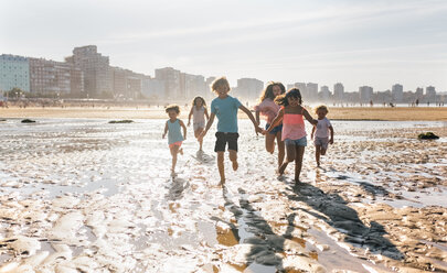 Group of six children running together on the beach - MGOF02847