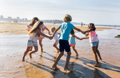 Gruppe von sechs Kindern spielt Ringelreihen am Strand - MGOF02851