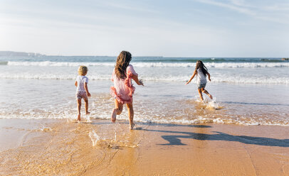 Rückenansicht von drei Kindern, die ins Meer laufen - MGOF02852