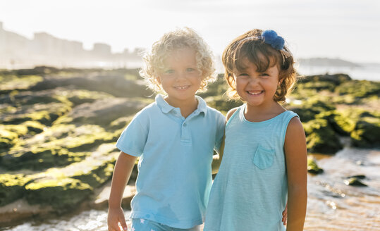 Porträt eines glücklichen kleinen Jungen und eines Mädchens Seite an Seite am Strand - MGOF02862