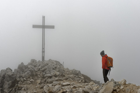 Italien, Südtirol, Mann am Gipfelkreuz des Weißhorns bei dichtem Nebel, lizenzfreies Stockfoto