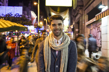 Portrait of smiling man in the city with unfocused people at night - ABZF01810