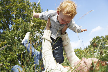 Mother lifting up happy son in meadow - FSF00664