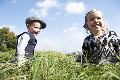 Zwei glückliche Kinder sitzen auf einer Wiese, lizenzfreies Stockfoto