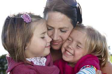 Mother hugging two girls outdoors - FSF00686