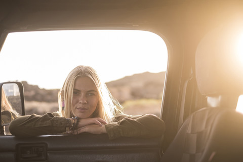 Porträt einer jungen Frau, die sich an ein Autofenster lehnt und hineinschaut, lizenzfreies Stockfoto
