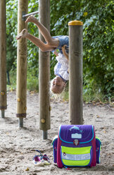 Smiling little girl with school bag on high bar of a playground - JFEF00834