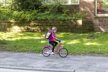 Smiling little girl with school bag riding bicycle on pavement - JFEF00838