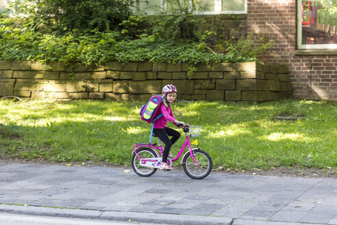 Lächelndes kleines Mädchen mit Schultasche auf dem Fahrrad auf dem Bürgersteig - JFEF00838