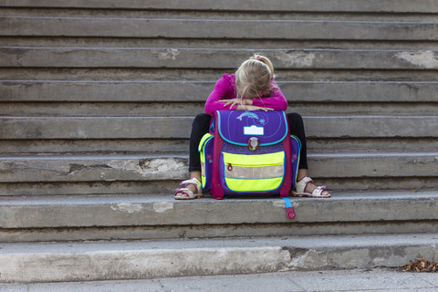 Trauriges kleines Mädchen sitzt mit Schultasche auf der Treppe, lizenzfreies Stockfoto