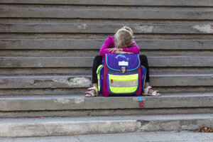 Sad little girl sitting on stairs with school bag - JFEF00839