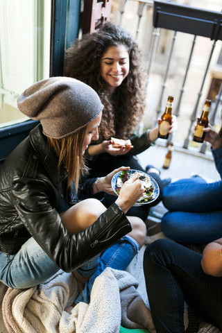 Group of friends sitting on the floor eating pizza and salad and drinking beer at home stock photo