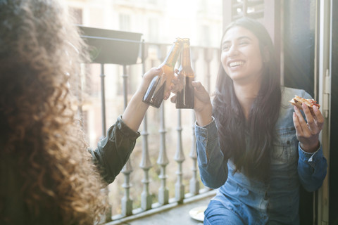 Lächelnde Frau stößt mit ihrer Freundin auf eine Bierflasche an, lizenzfreies Stockfoto