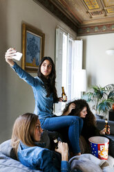 Young woman with beer bottle taking a selfie while seating on the couch with her friends - VABF01086