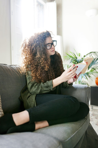 Young woman wearing glasses sitting on couch reading book stock photo