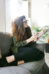Young woman wearing glasses sitting on couch reading book - VABF01088