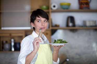 Porträt einer jungen Frau, die in der Küche Salat probiert - SGF02103