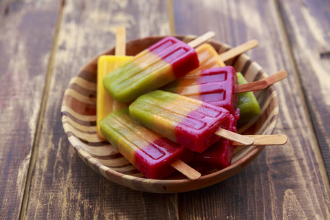 Wooden bowl of homemade fruit smoothie ice lollies on wood stock photo