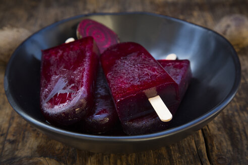 Bowl of homemade beetroot ice lollies on wood - LVF05833