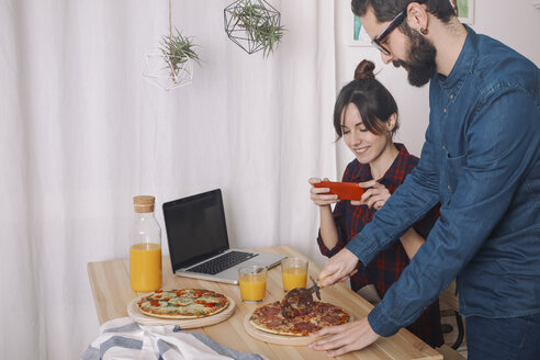 Junges Paar isst Pizza und trinkt Saft zum Mittagessen, Frau macht Fotos mit Smartphone - RTBF00622