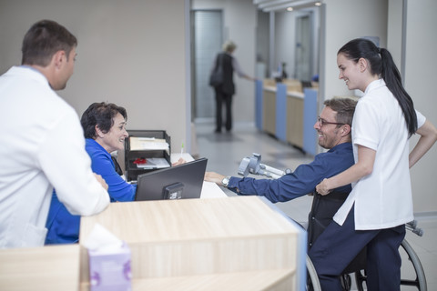 Patient im Rollstuhl sitzend im Gespräch mit dem Personal an der Rezeption, lizenzfreies Stockfoto