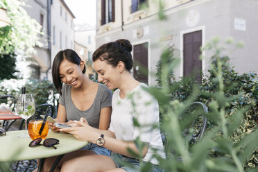 Italy, Padua, two young women checking their cell phones at sidewalk cafe - ALBF00072