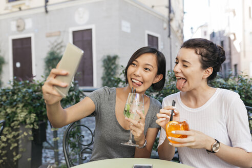 Italy, Padua, two young women pulling funny faces while taking selfie at sidewalk cafe - ALBF00074