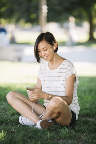 Smiling young woman sitting on a meadow listening music with earphones stock photo