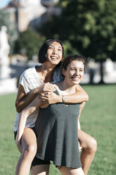 Young woman giving her friend a piggyback ride in the park - ALBF00108