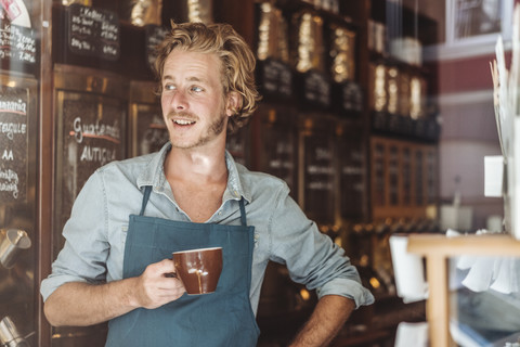 Lächelnder Kaffeeröster in seinem Laden und trinkt eine Tasse Kaffee, lizenzfreies Stockfoto