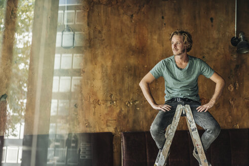 Man sitting on stepladder in unfinished room - KNSF00925