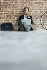 Businessman sitting on floor using laptop and cell phone - KNSF00931