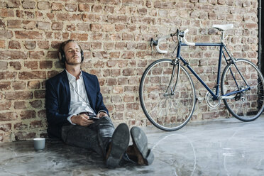 Relaxed man with headphones leaning against brick wall - KNSF00932