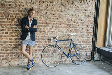 Smiling businessman standing at brick wall wearing jacket and underwear - KNSF00936