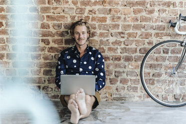 Man sitting at brick wall using laptop - KNSF00967