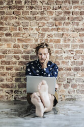 Man sitting at brick wall using laptop - KNSF00969